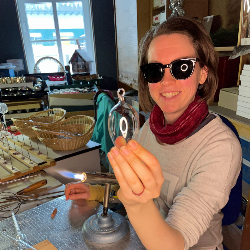 Frau am Brenner hält ein Ei aus Glas geblasen in der Hand